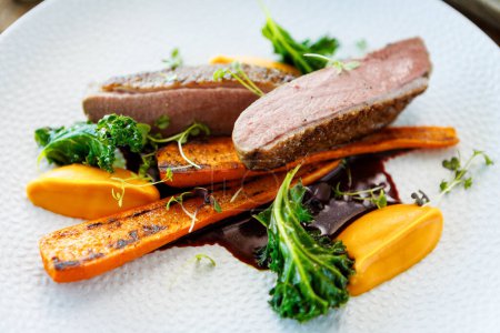 Photo for Duck fillet with sweet potato cream, roasted carrots, kale, beet-port sauce on white plate. Grilled and roasted poultry closeup served on a table for lunch in modern cuisine gourmet restaurant - Royalty Free Image