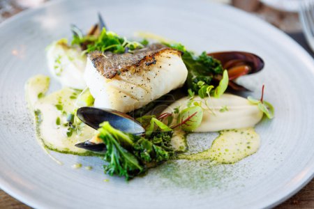 Photo for Cod fillet with cauliflower cream, asparagus, clam-wine sauce and mussles. Delicious seafood fish closeup served on a table for lunch in modern cuisine gourmet restaurant. - Royalty Free Image