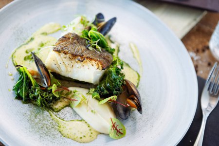 Cod fillet with cauliflower cream, asparagus, clam-wine sauce and mussles. Delicious seafood fish closeup served on a table for lunch in modern cuisine gourmet restaurant.