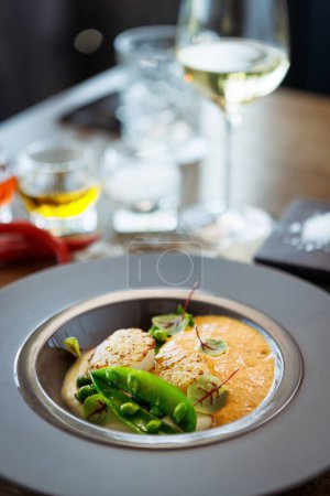 Foto de Vieiras con espuma de camarón, crema de coliflor y guisantes verdes en un plato. Delicioso primer plano de mariscos saludables servido para el almuerzo en una mesa en el restaurante de cocina gourmet moderna. - Imagen libre de derechos