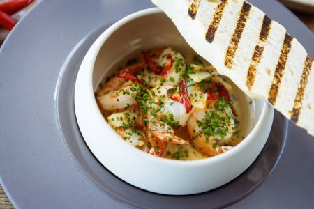 Photo for Shrimp pil-pil. King prawns, garlic, chilli and baguette. Delicious Spanish traditional food closeup served for lunch in modern gourmet cuisine restaurant. - Royalty Free Image