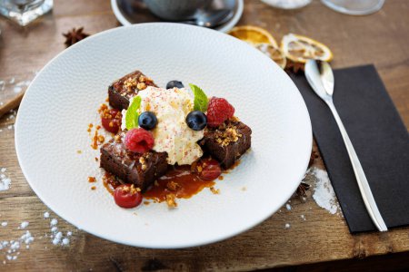 Photo for Brownie cake with salted caramel. Anglaise foam, raspberry sauce, praline nut and fresh berry. Delicious sweet dessert food closeup served for lunch in modern gourmet cuisine restaurant. - Royalty Free Image