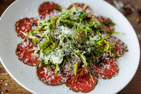 Photo for Beef carpaccio. Borettane onion, sun-dried tomato, truffle dressing, arugula salad, parmesan cheese. Italian traditional antipasti snacks served for lunch with wine in modern gourmet restaurant. - Royalty Free Image