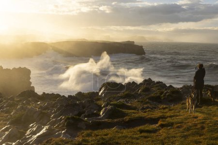 Foto de Mujer tomando una foto de la costa del océano en Bufones de Pria en Asturias al norte de España en un día ventoso con mar agitado y olas - Imagen libre de derechos