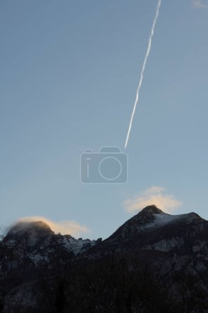Vertikale Landschaft von Flugzeugen, die über Berggipfel fliegen, mit Nebel bei Sonnenuntergang im Winter.