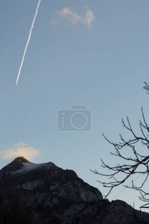 Vertical landscape of airplane flying above mountain peaks with fog at sunset in winter.