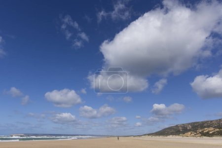 Turista caminando por la playa en la orilla del Mediterráneo en Zahara de los Atunes en un día de verano con cielo azul y nubes.
