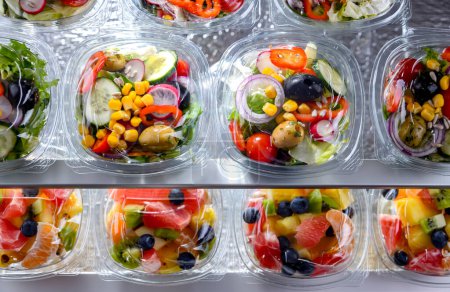 Téléchargez les photos : Boîtes en plastique avec salades de légumes préemballées, conditionnées pour la vente au réfrigérateur commercial - en image libre de droit