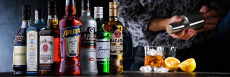 Foto de POZNAN, POL - DIC 28, 2021: Botellas de varias marcas mundiales de licores duros y un camarero que prepara una bebida con una coctelera - Imagen libre de derechos