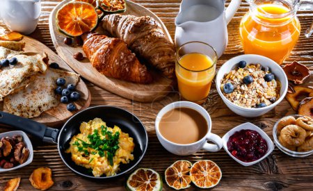 Photo for Breakfast served with coffee, orange juice, scrambled eggs, cereals, pancakes and croissants. - Royalty Free Image