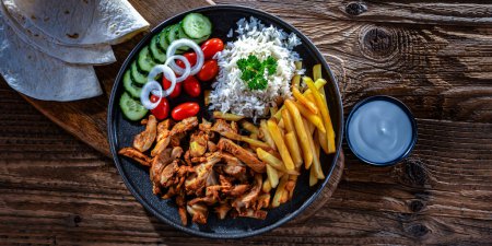 Foto de Kebab servido con arroz, papas fritas, pan de pitta, verduras y tzatziki - Imagen libre de derechos