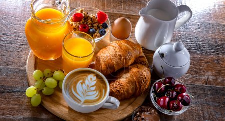 Foto de Desayuno servido con café, zumo de naranja, huevo, cereales y cruasanes. - Imagen libre de derechos