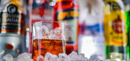 Foto de POZNAN, POL - 29 NOV 2023: Un vaso de bebida alcohólica sobre botellas de licor duro de marcas mundiales en un bar - Imagen libre de derechos
