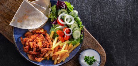 Foto de Kebab servido con papas fritas, pan de pitta, verduras y tzatziki - Imagen libre de derechos