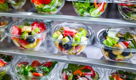 Foto de Cajas de plástico con ensaladas de frutas y verduras preenvasadas, puestas a la venta en un refrigerador comercial - Imagen libre de derechos