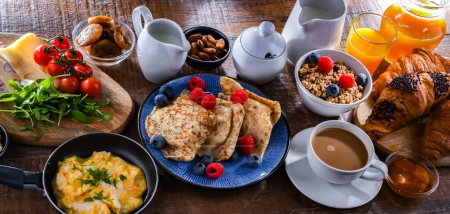 Téléchargez les photos : Breakfast served with coffee, orange juice, scrambled eggs, cereals, pancakes and croissants. - en image libre de droit