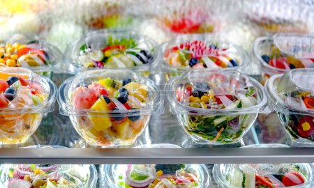 Foto de Plastic boxes with pre-packaged fruit and vegetable salads, put up for sale in a commercial refrigerator - Imagen libre de derechos