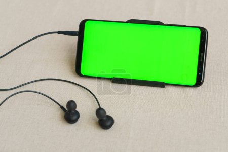 Téléchargez les photos : Écouteurs et téléphone portable avec écran vert. - en image libre de droit