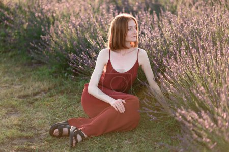 Photo for A red-haired young girl without make-up is resting in a lavender field. Summer vacation and travel time. - Royalty Free Image