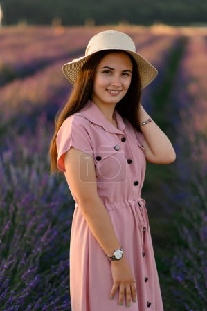 Photo for Cheerful young girl in a straw hat and pink dress on the background of a lavender field. Sunset. - Royalty Free Image