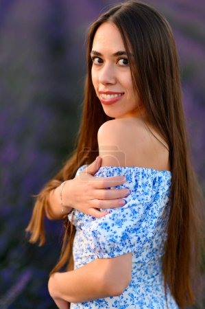 Photo for Attractive slender happy girl in a blue dress in a lavender field at sunset. - Royalty Free Image