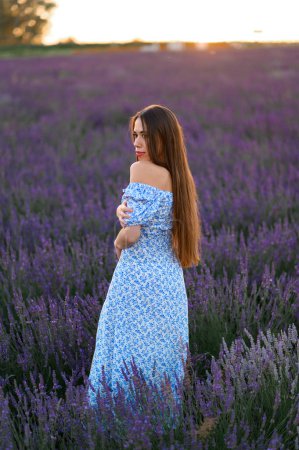 Photo for Attractive slender happy girl in a blue dress in a lavender field at sunset. - Royalty Free Image