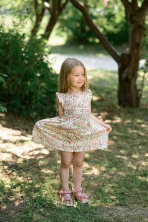 Photo for Little girl 3 years old in a summer sundress in the park. Summer time. The little girl clumsily lifted her dress - Royalty Free Image
