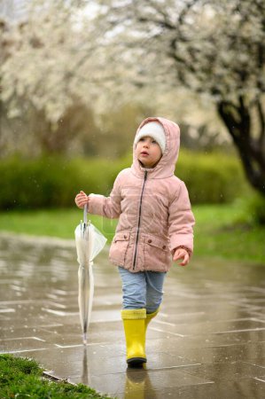 Photo for A little girl 3 years old walks in yellow rubber boots, after the rain. The girl looks away. - Royalty Free Image