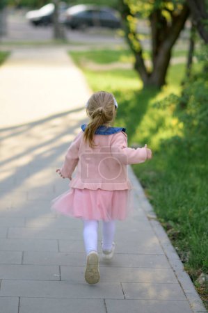 Photo for A little girl 3 years old in a summer dress runs away from the camera. The girl is turned back. Summer time. - Royalty Free Image