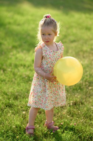 Photo for Little girl 3 years old in a summer dress in a clearing with an yellow ball in her hands. The girl is not happy - Royalty Free Image