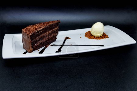Téléchargez les photos : Composition d'un gâteau au chocolat sur une assiette blanche avec crème glacée sur fond noir - en image libre de droit
