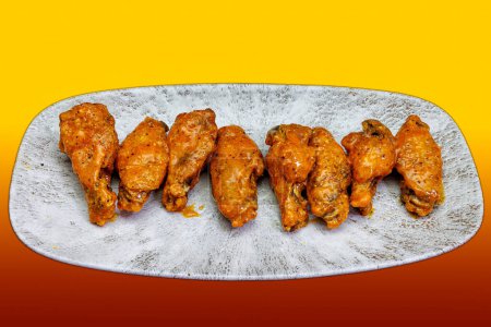 Foto de Composición de un plato de alitas de pollo con salsa Buffalo sobre un fondo rojo y amarillo - Imagen libre de derechos