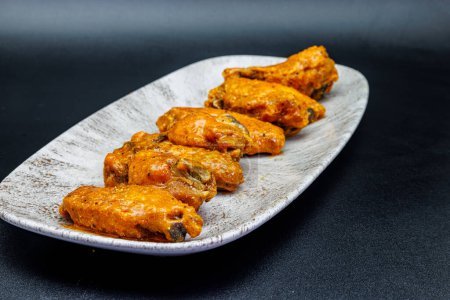 Téléchargez les photos : Composition d'une assiette d'ailes de poulet avec sauce Buffalo sur fond noir. - en image libre de droit