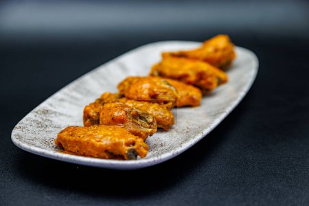 Photo for Composition of a plate of chicken wings with Buffalo sauce on a black background. - Royalty Free Image