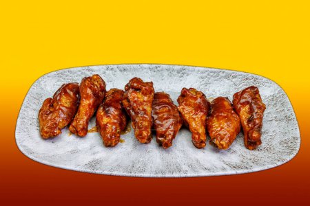 Photo for Composition of a plate of chicken wings with BBQ sauce on a yellow and red gradient background - Royalty Free Image