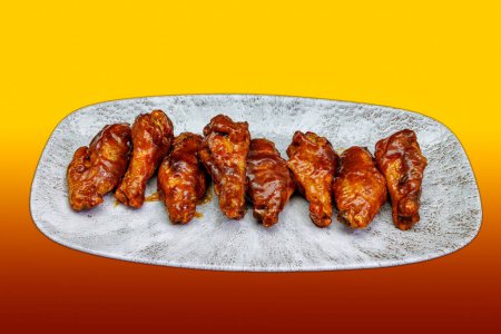 Téléchargez les photos : Composition d'une assiette d'ailes de poulet avec sauce barbecue sur fond dégradé jaune et rouge - en image libre de droit