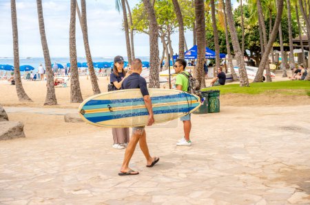 Foto de Honolulu, Hawaii - December 31,  2022: Young man carrying rental surfboard to the ocean on Waikiki Beach. - Imagen libre de derechos
