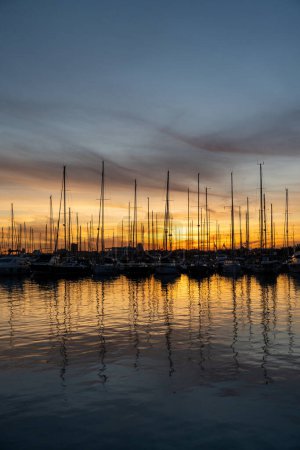 Téléchargez les photos : Yachts avec reflet dans l'eau de mer du port de Valence. Des grues portuaires à l'horizon. Soirée chaude en Espagne. - en image libre de droit