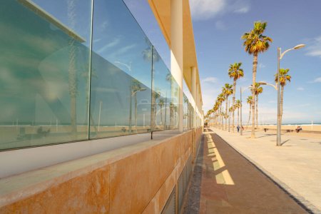 Foto de Paseo marítimo en la playa de arena del Mediterráneo en primavera. La playa y los turistas se reflejan en la fachada de cristal del edificio. Valencia - Imagen libre de derechos