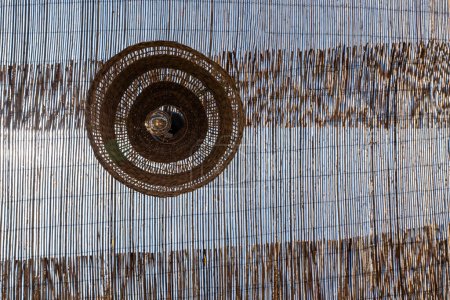 Foto de Lámpara con pantalla redonda de mimbre. Sobre el fondo de un tejado transparente de mimbre. España - Imagen libre de derechos