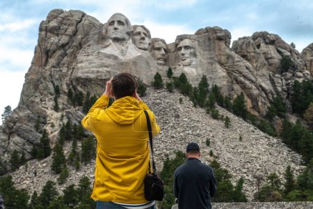 Tourists taking pictures and observe mountain Rushmor with USA presidents sculptures.