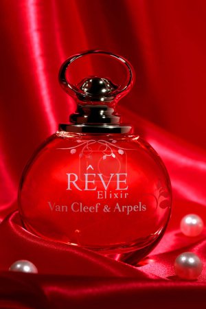 Foto de Botella de perfume .reve elixir van cleef & arpels y perlas sobre fondo de seda roja - Imagen libre de derechos