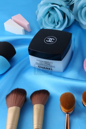 Téléchargez les photos : Chanel gel crème hydra beauté avec accessoires de maquillage, brosses et éponges sur soie, fond bleu - en image libre de droit