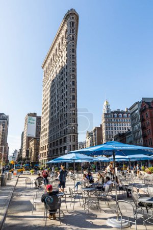 Téléchargez les photos : NEW YORK, États-Unis - 5 OCT 2017 : les gens aiment s'asseoir à Broadwayon chaises publiques avec wlan gratuit et regardant vers la façade spectaculaire du bâtiment Flatiron. - en image libre de droit