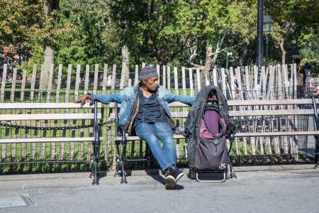 Téléchargez les photos : NEW YORK, États-Unis - 5 OCT 2017 : Un pauvre sans-abri assis sur un banc avec son sac à dos et ses vêtements. Le nombre de sans-abri s'accroît de plus de 15 % au cours des 5 dernières années. - en image libre de droit