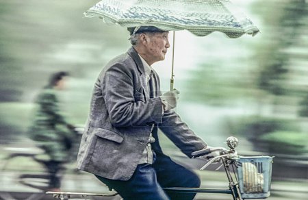 Téléchargez les photos : Pékin, Chine - 1er août 1982 : le vieil homme fait du vélo avec son parapluie dans le bras. I 1982 vélo était pour plus de 95 pour cent des Chinois le moyen de transport, même à Pékin. - en image libre de droit