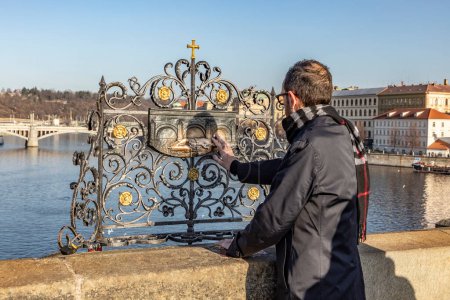 Foto de Praga, República Checa - 1 de enero de 2020: Mano del hombre en el marco, persona frotando la placa de bronce en el puente de Carlos, pidiendo un deseo. - Imagen libre de derechos