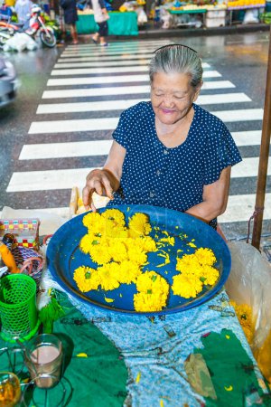 Foto de Bangkok, Tailandia - 12 de mayo de 2009: mujer mayor vende flores sagradas de color naranja a la gente local en el mercado nocturno Pak khlong Talat en Chinatown, Bangkok. - Imagen libre de derechos