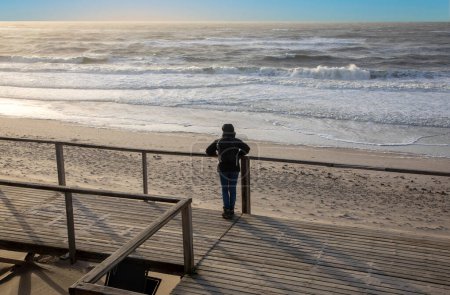 Téléchargez les photos : Lonely woman watches the waves at the ocean at an empty beach in autumn at sunset - en image libre de droit