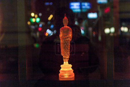 Téléchargez les photos : Vienna, Austria - December 5, 2009: colorful buddha statue in a shop with reflection of street light in glass window by night. - en image libre de droit